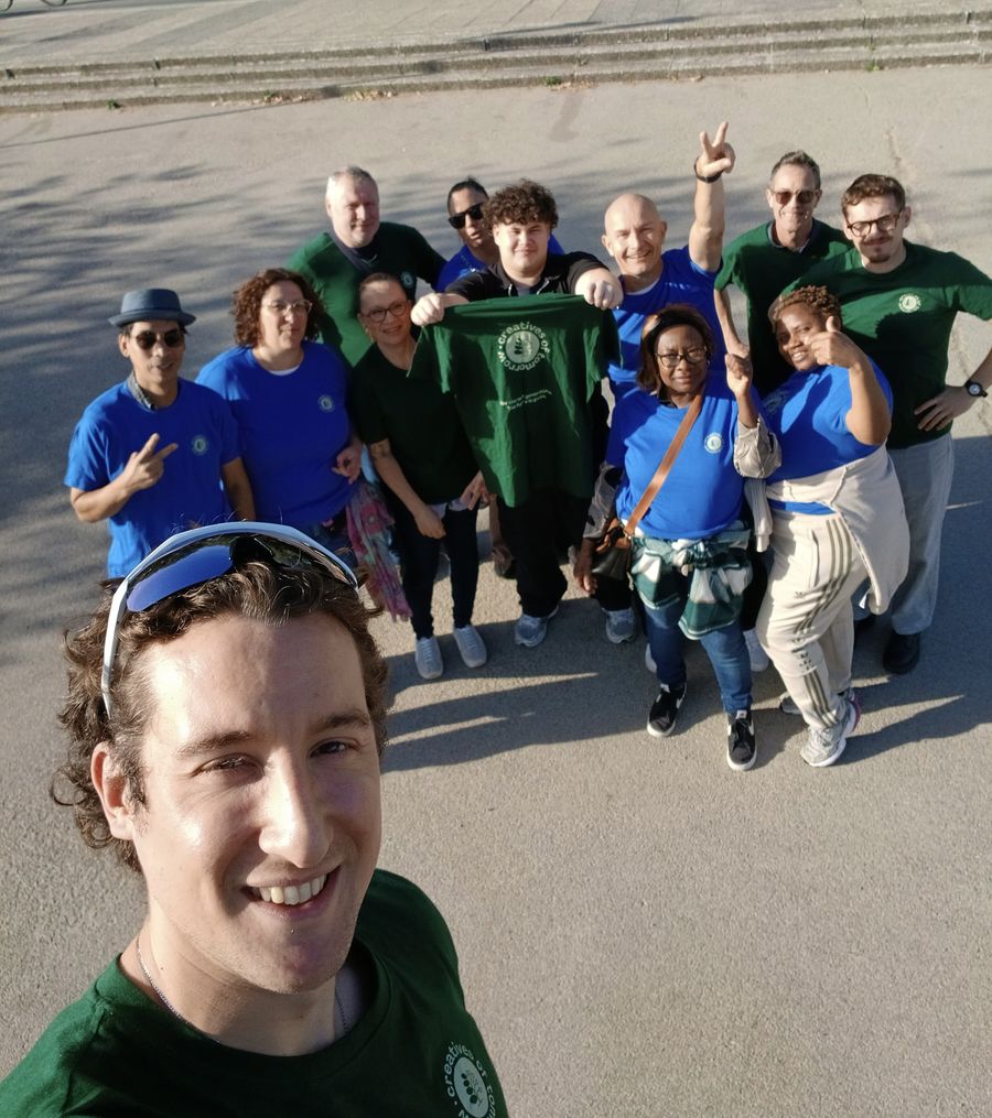 A Creatives of Tomorrow volunteer takes a selfie with a group of volunteers in blue and green T-shirts, one holding up a Creatives of Tomorrow T-shirt