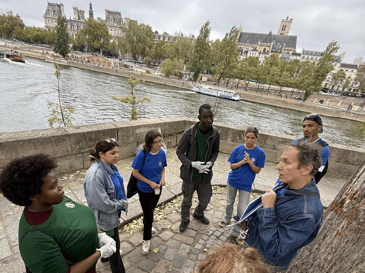 Creatives of Tomorrow volunteers gathered in a circle by the Seine, listening to a speaker, with the Hôtel de Ville in the background