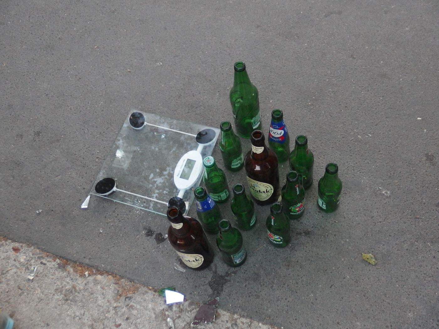 Glass bottles and discarded items collected during a cleanup, sorted on the pavement